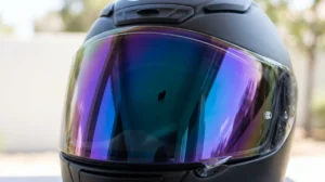 Visière de casque moto iridium teintée légale, reflets bleus et violets sur fond neutre.